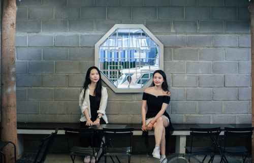 Free Two women sitting on a bench in a trendy cafe with a unique mirror on the wall. Stock Photo