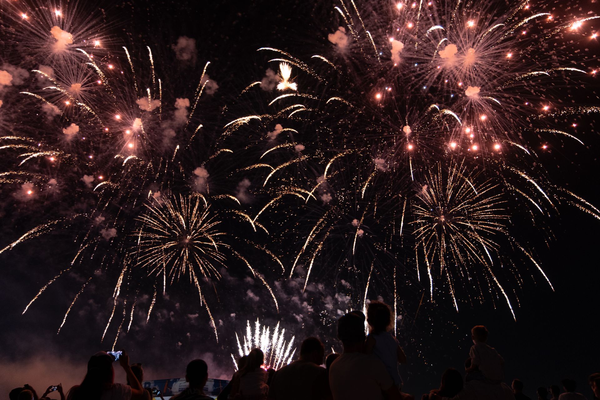 Silhouetted crowd watching a brilliant fireworks display lighting up the night sky.