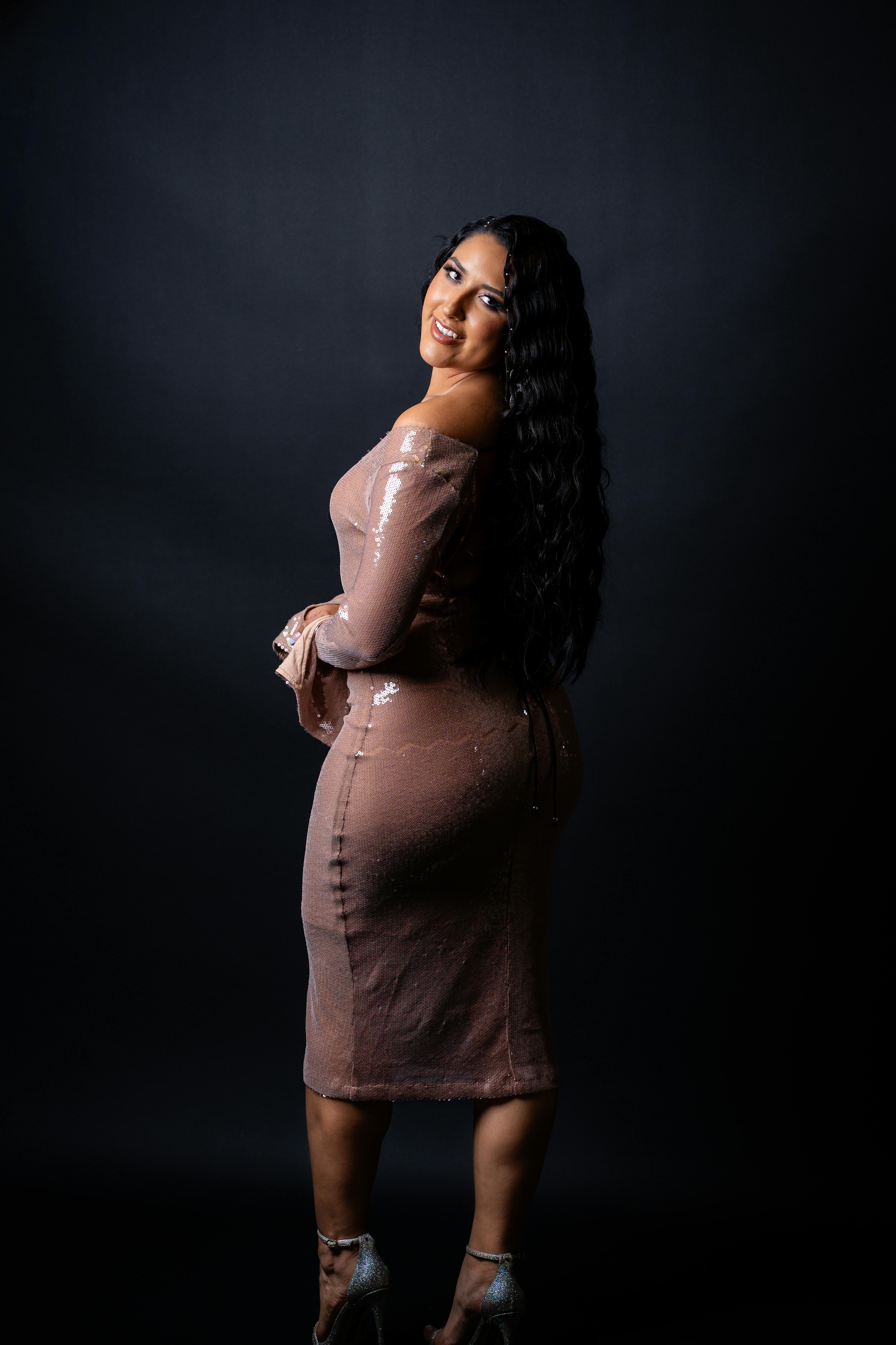 Woman in pink sequin dress posing confidently against dark backdrop.