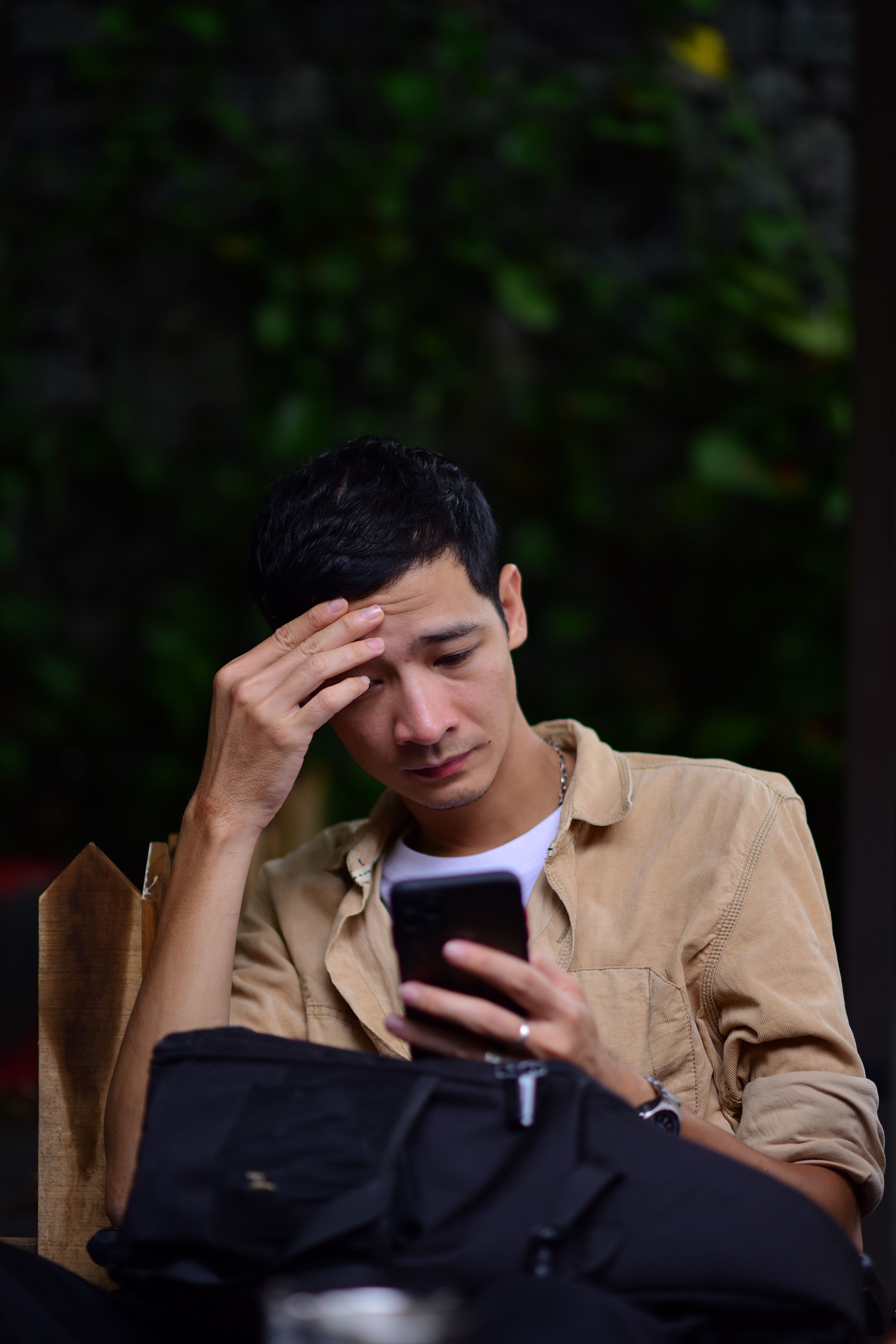 A young man looks stressed while checking his smartphone outdoors, possibly receiving bad news.