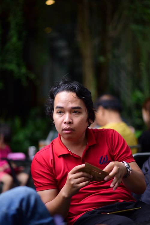Free Young man in a red shirt holding his phone, seated in an outdoor cafe setting. Stock Photo