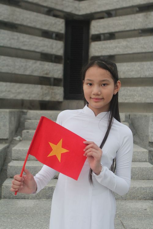 Free Young girl in white outfit holding Vietnam flag on stone steps. Stock Photo