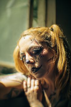 Close-up of woman with dramatic clown makeup in a dimly lit room, exuding a mysterious and creative vibe.