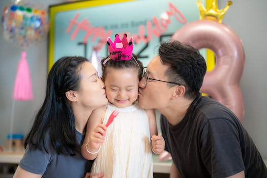 A cheerful moment of parents kissing their child during a birthday party indoors.