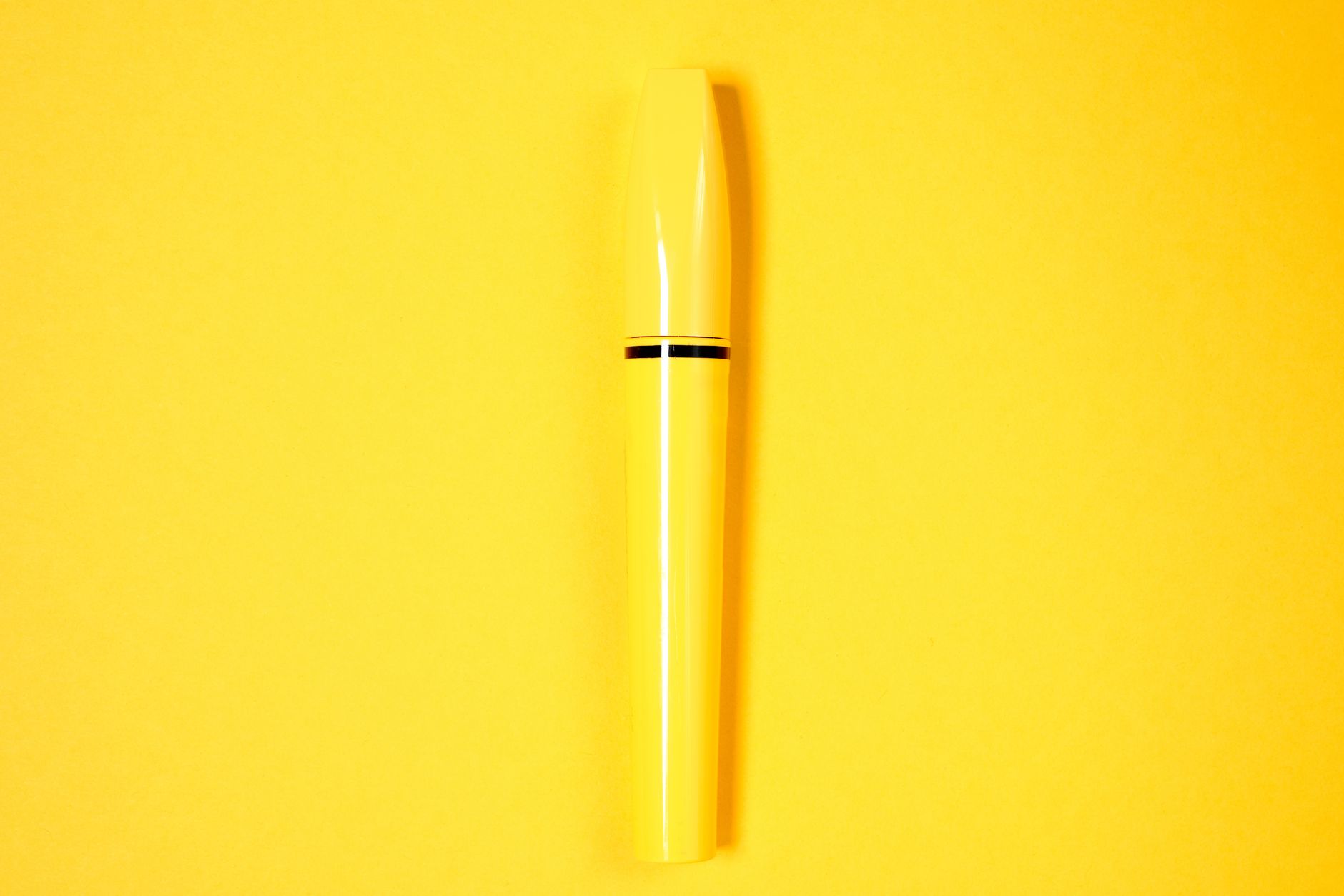 Minimalist yellow mascara tube displayed on a vibrant yellow background.