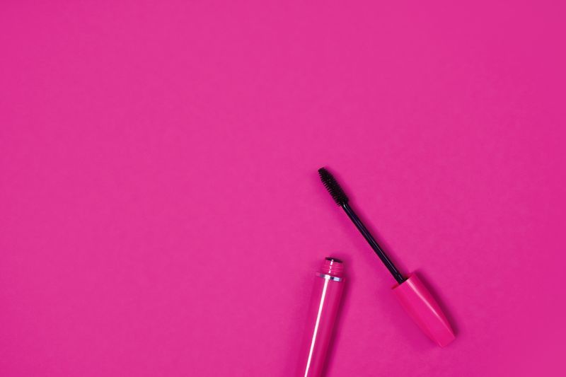 Open mascara tube and wand on a pink background