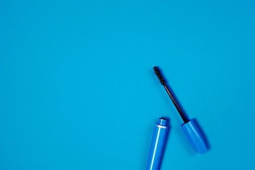 蓝色睫毛膏管和画笔在充满活力的蓝色背景上的特写