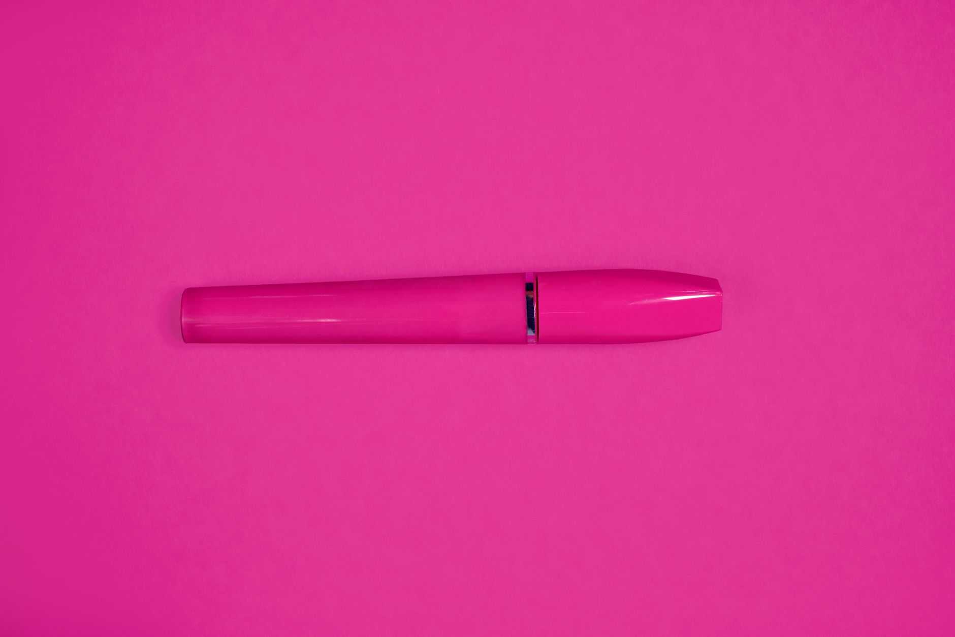 A bright pink mascara tube set against a matching pink background, perfect for beauty product marketing.