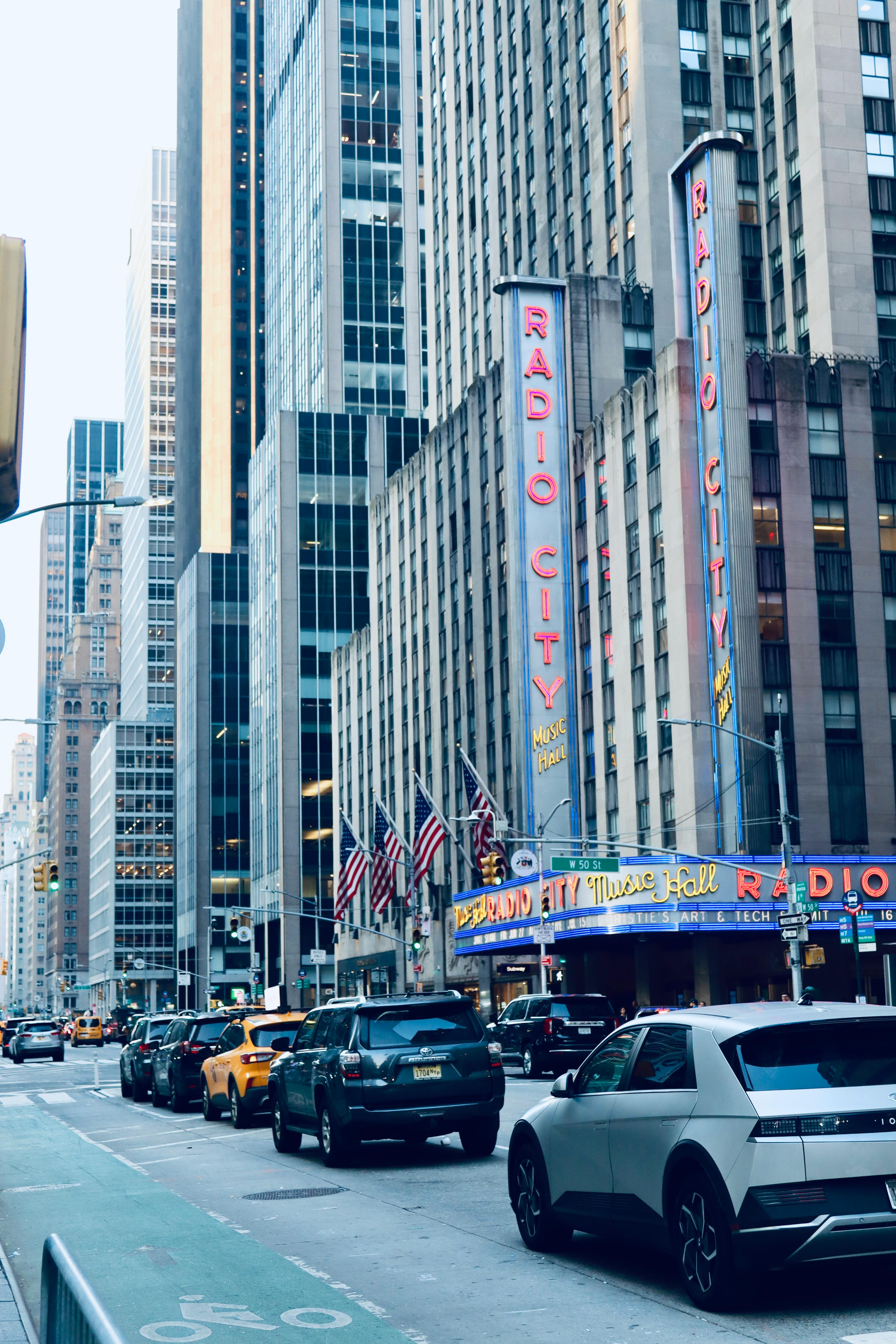Free Street view of Radio City Music Hall with cars and skyscrapers in New York City. Stock Photo