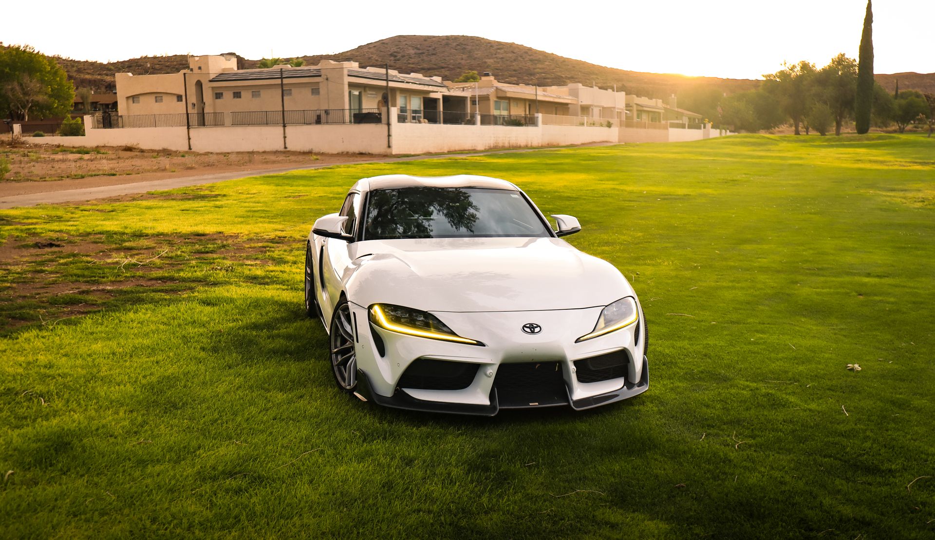 White sports car on green grass field with sunlight in suburban area.