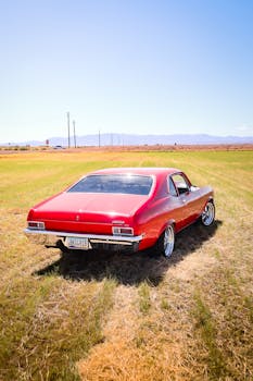 Classic red vintage car parked on grass on a sunny day, showcasing retro automotive style.