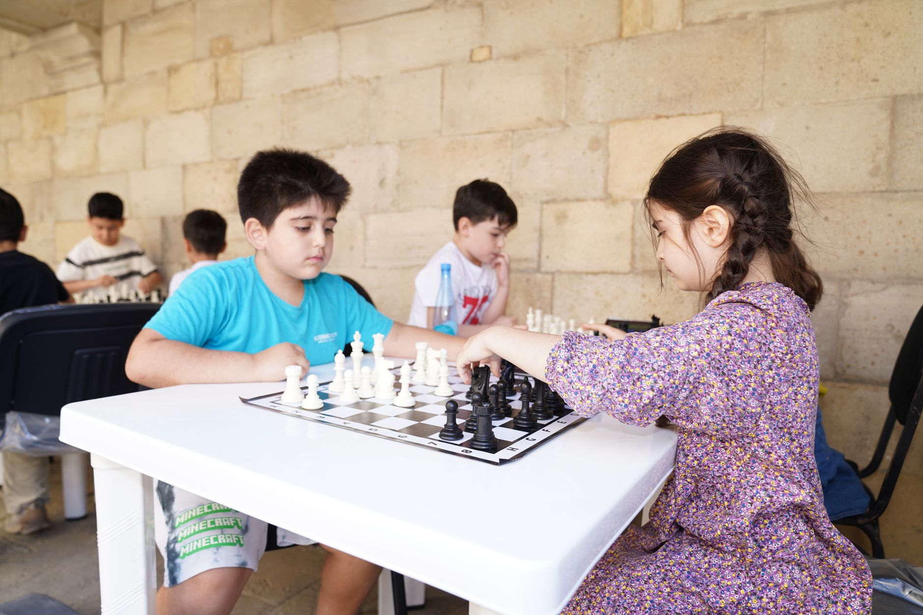 university fresher week entertainment Egypt — Young children engage in a chess match at an outdoor table, focusing intently o