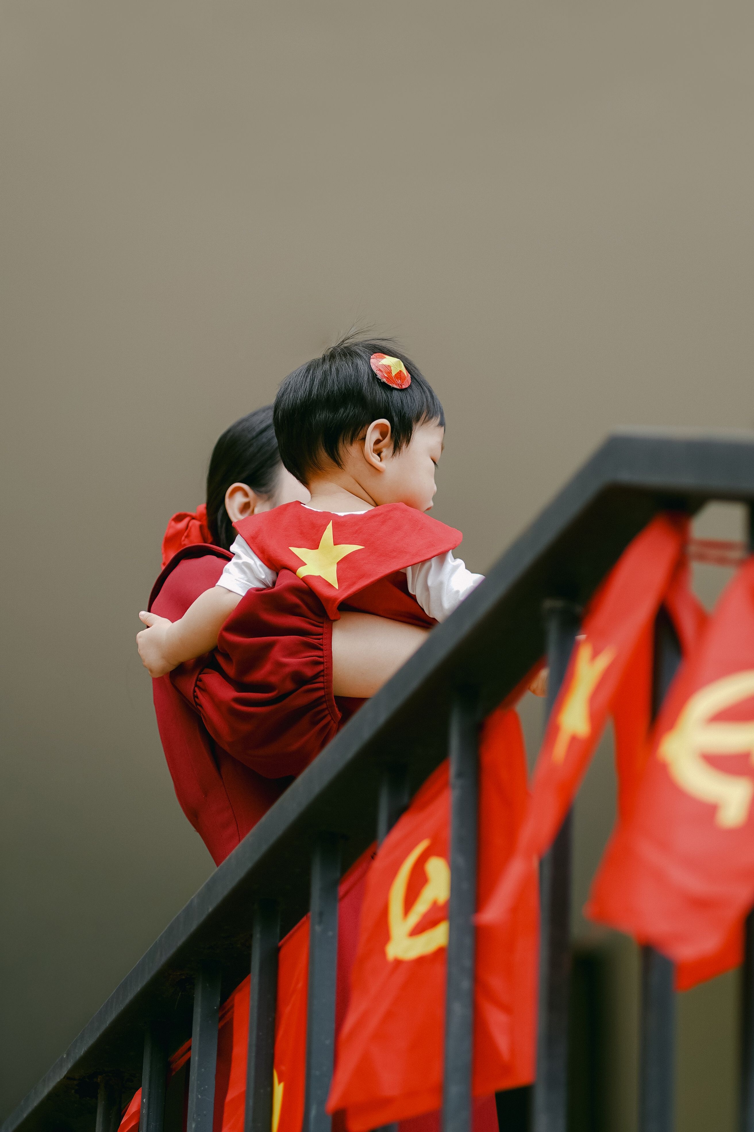 Ibu dan anak berpakaian merah dengan bendera bergambar bintang dan simbol kuning, melambangkan patriotisme. Via Pexels (by THONG NGUYEN)