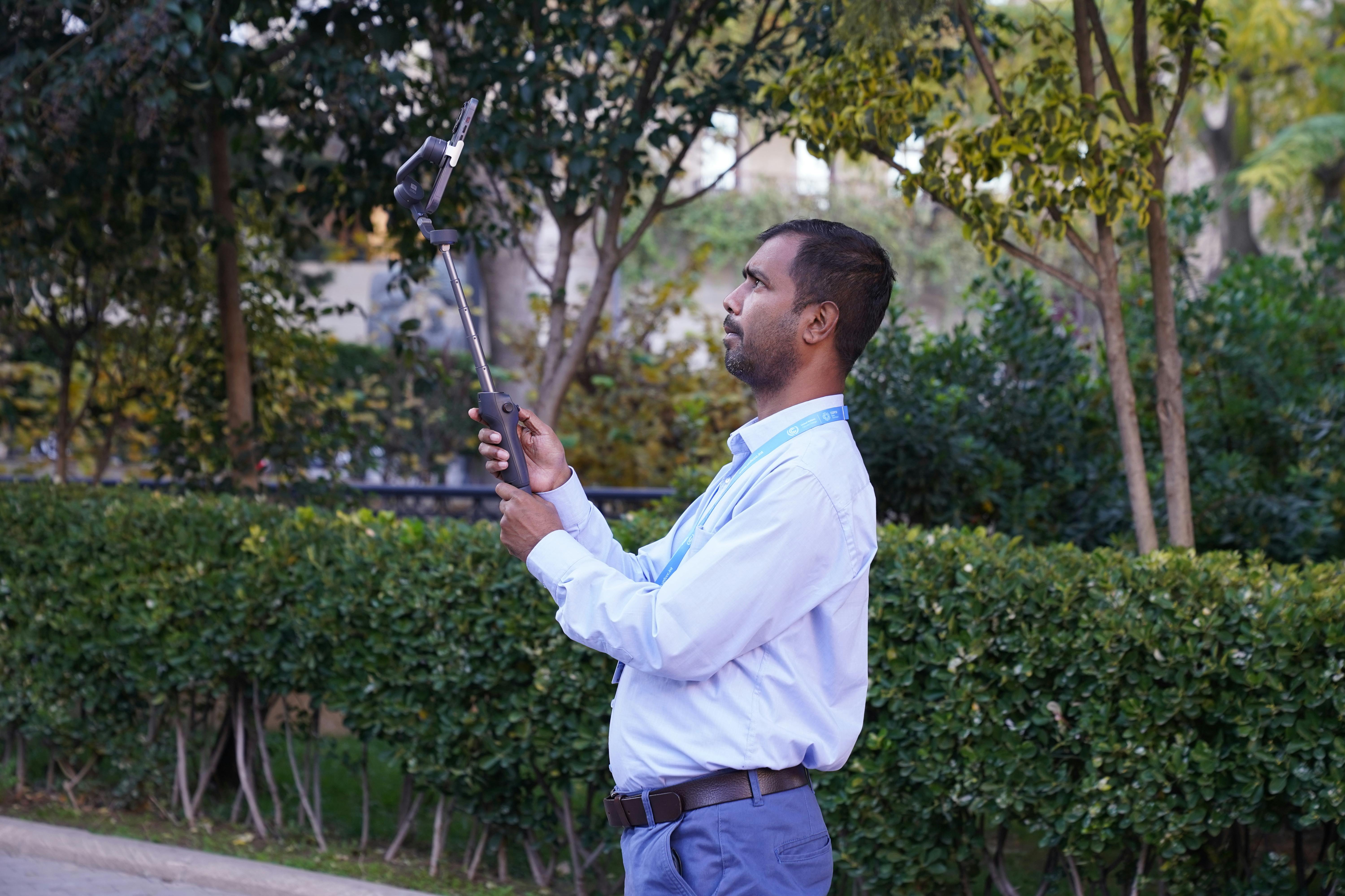 Free A man taking a selfie with a stick in a lush green park, capturing the beauty of nature. Stock Photo