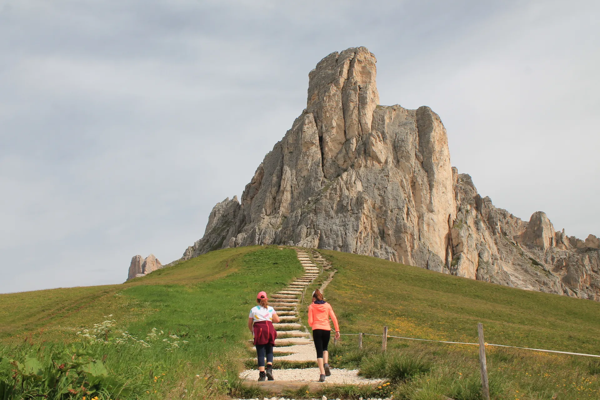 Two women hiking a mountain trail toward a high pass in the Dolomites Two women hiking a mountain trail toward a high pass in the Dolomites