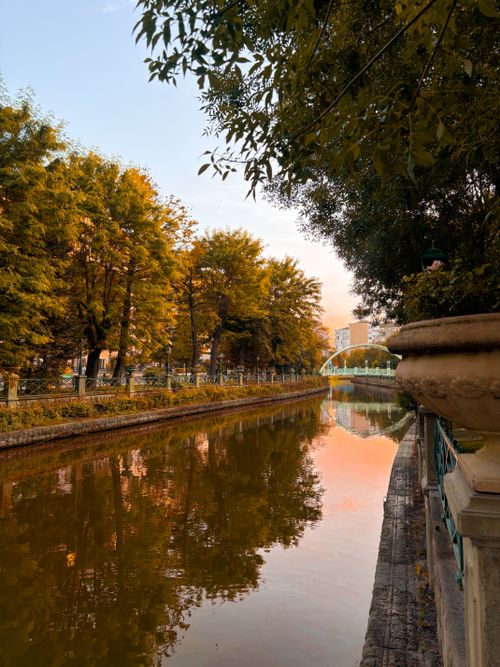 Free Tranquil autumn view of a canal lined with trees and a distant bridge at sunset. Stock Photo