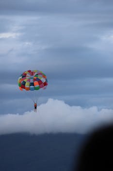 A vibrant parasailing scene with a person soaring through the cloudy sky.