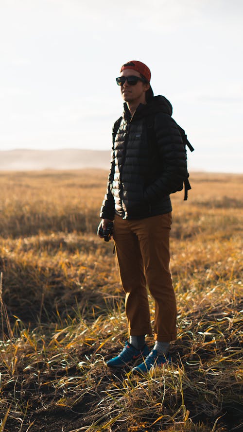 無料 茶色の草の上に立っている黒いフード付きジャケットを着ている男 写真素材