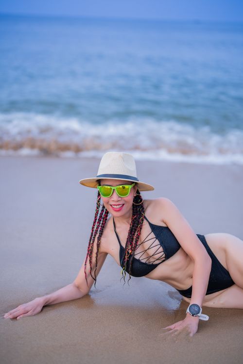 Free Woman in bikini and hat posing on beach with ocean backdrop. Stock Photo