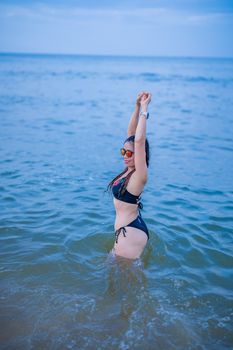 Woman in a bikini enjoying the ocean water on a bright day, stretching her arms.