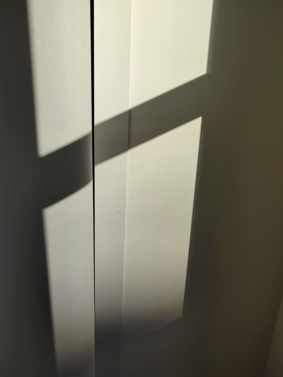 A minimalist composition showcasing sunlight casting geometric shadows on a wall, conveying simplicity and warmth.