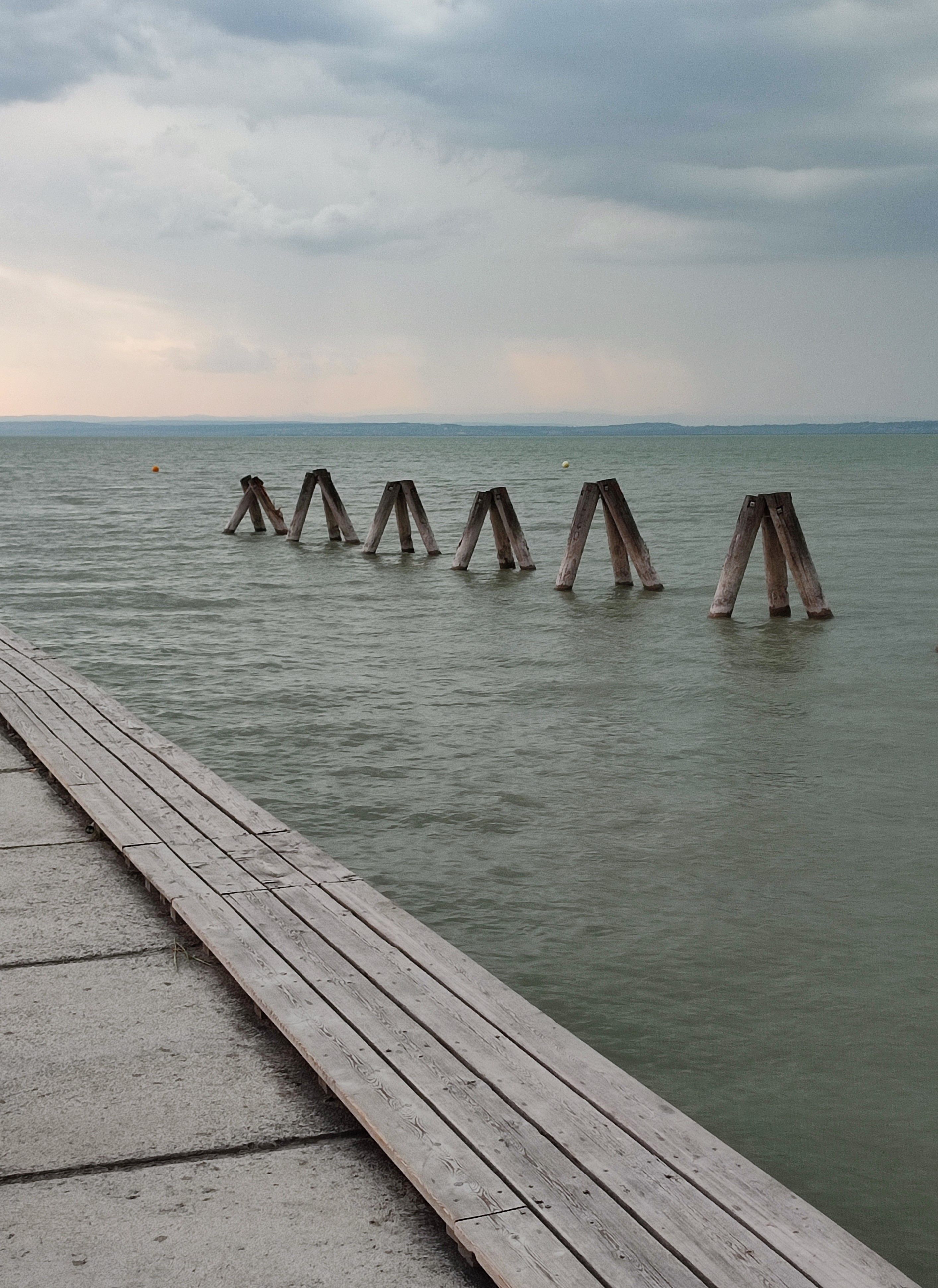 grátis Uma vista serena de um cais que se estende até o Lago Neusiedl sob um céu nublado, capturando uma sensação de paz. Foto profissional