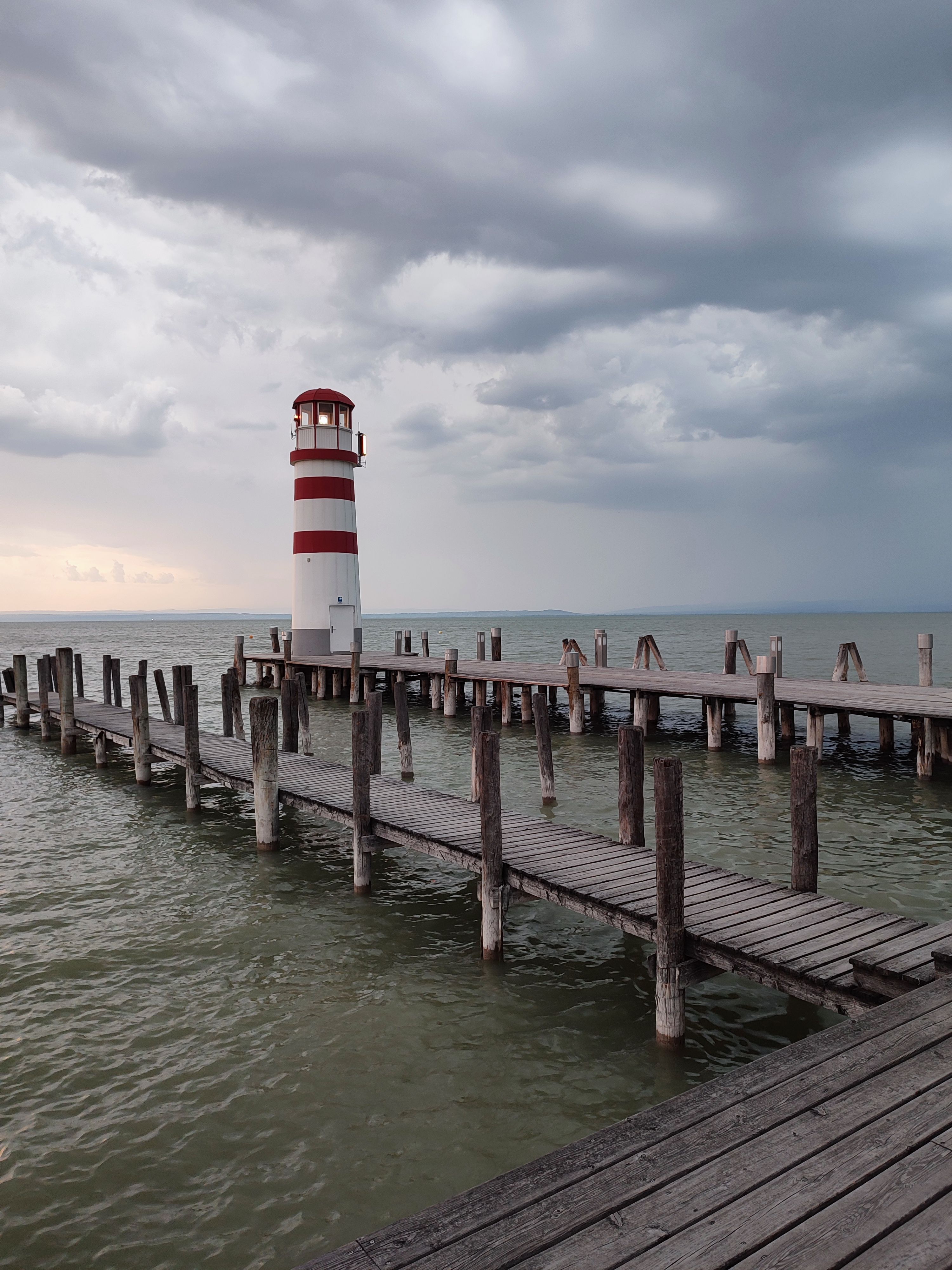 grátis Um farol pitoresco em um píer de madeira com um céu dramático, perfeito para viagens e temas de natureza. Foto profissional