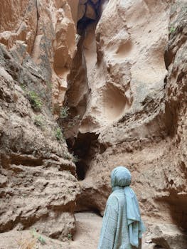 A person in a hijab explores a stunning rocky canyon with towering cliffs.