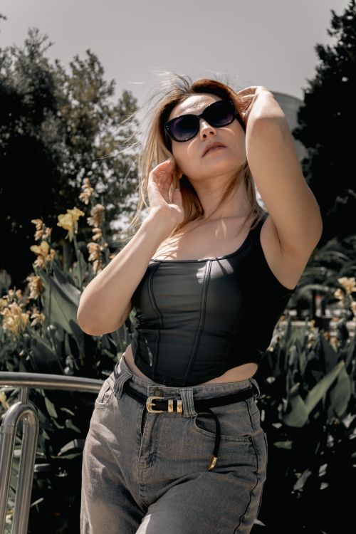 Free Stylish woman in sunglasses posing confidently with greenery in background. Stock Photo