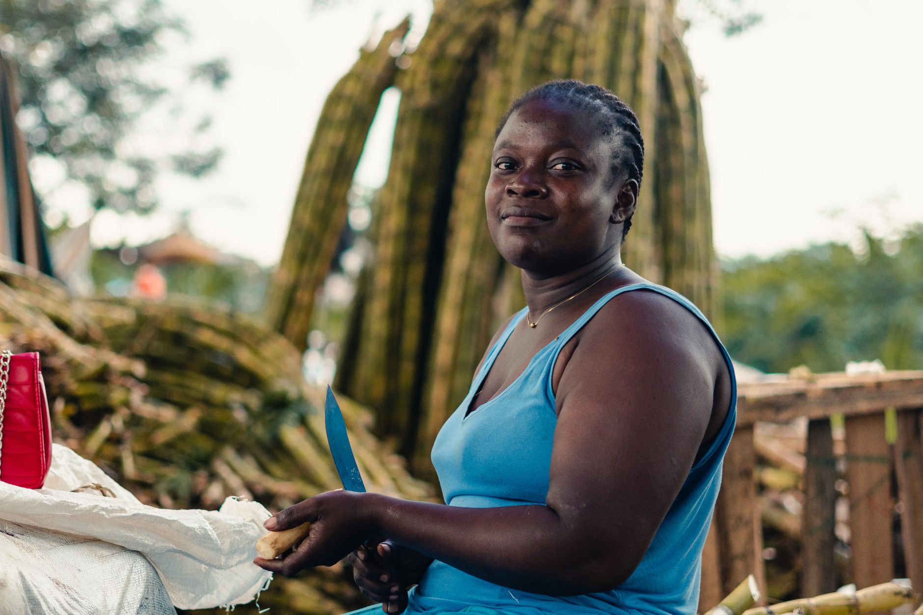 A woman in a blue tank top prepares food with a knife against a natural outdoor backdrop.