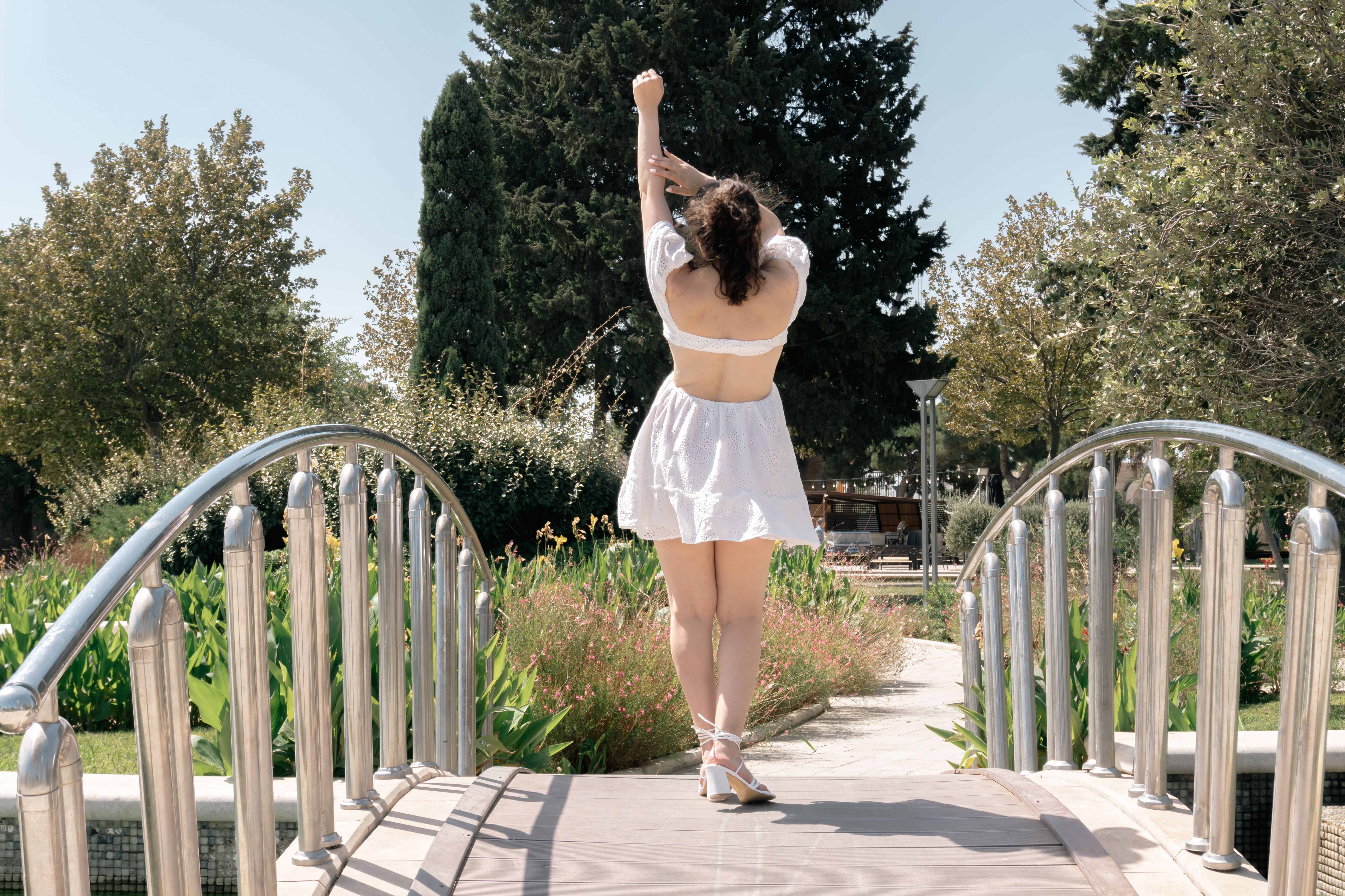 Une jeune femme en robe blanche s'étire sur un charmant pont de jardin sous le soleil d'été.