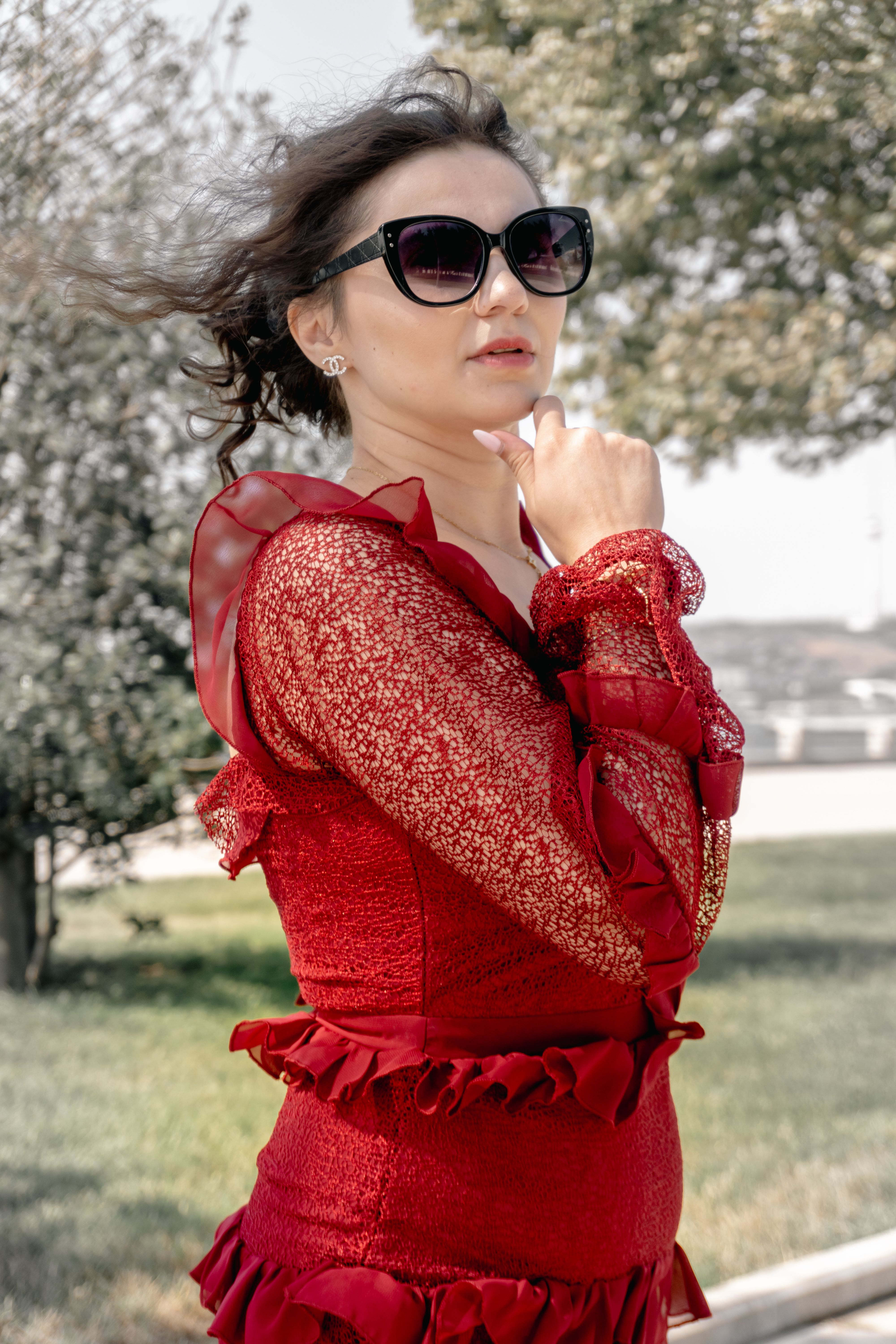 Stylish woman wearing sunglasses and a red dress stands confidently outdoors in a breezy setting.