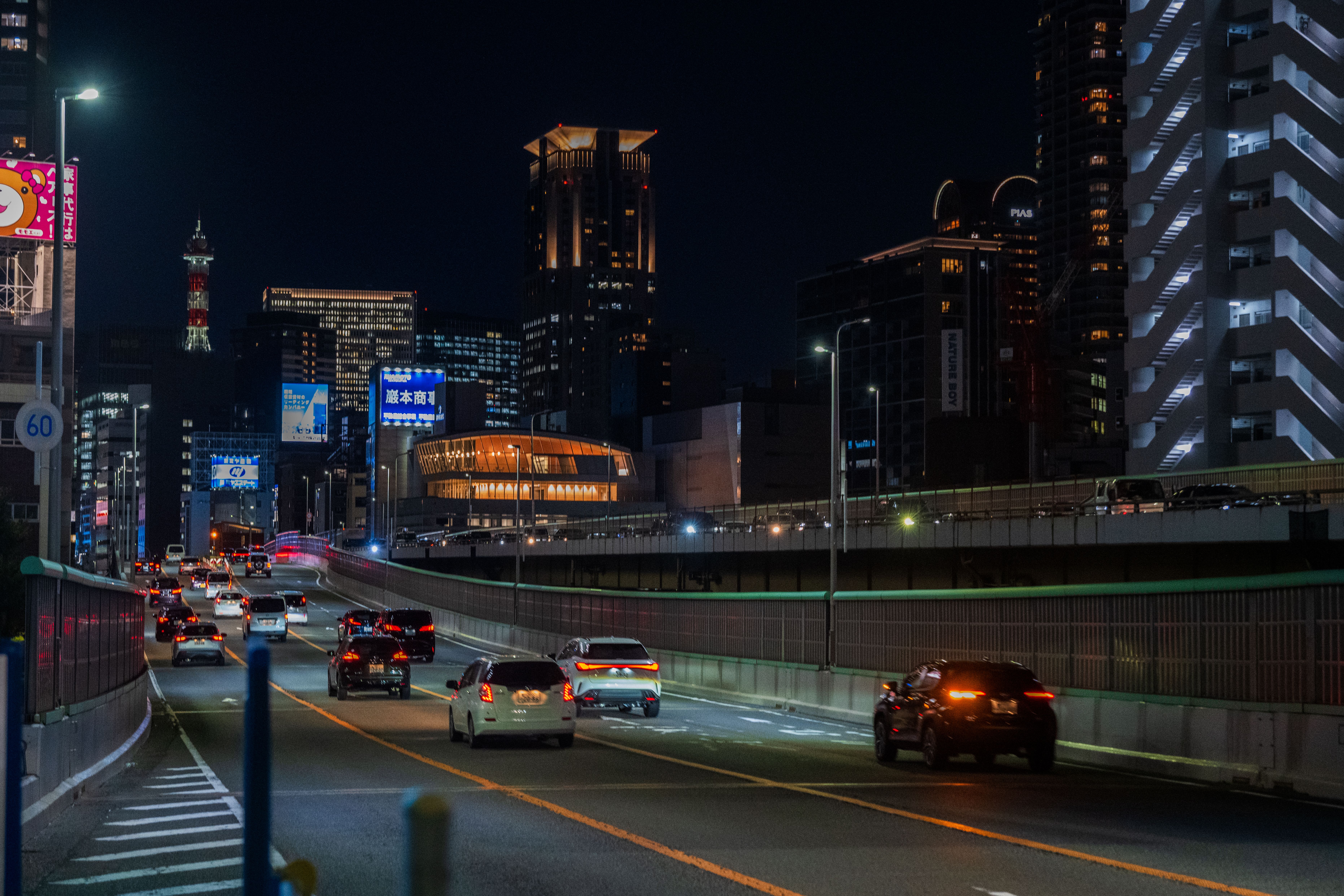 Cars driving on a highway at night with a vibrant city skyline in the background.