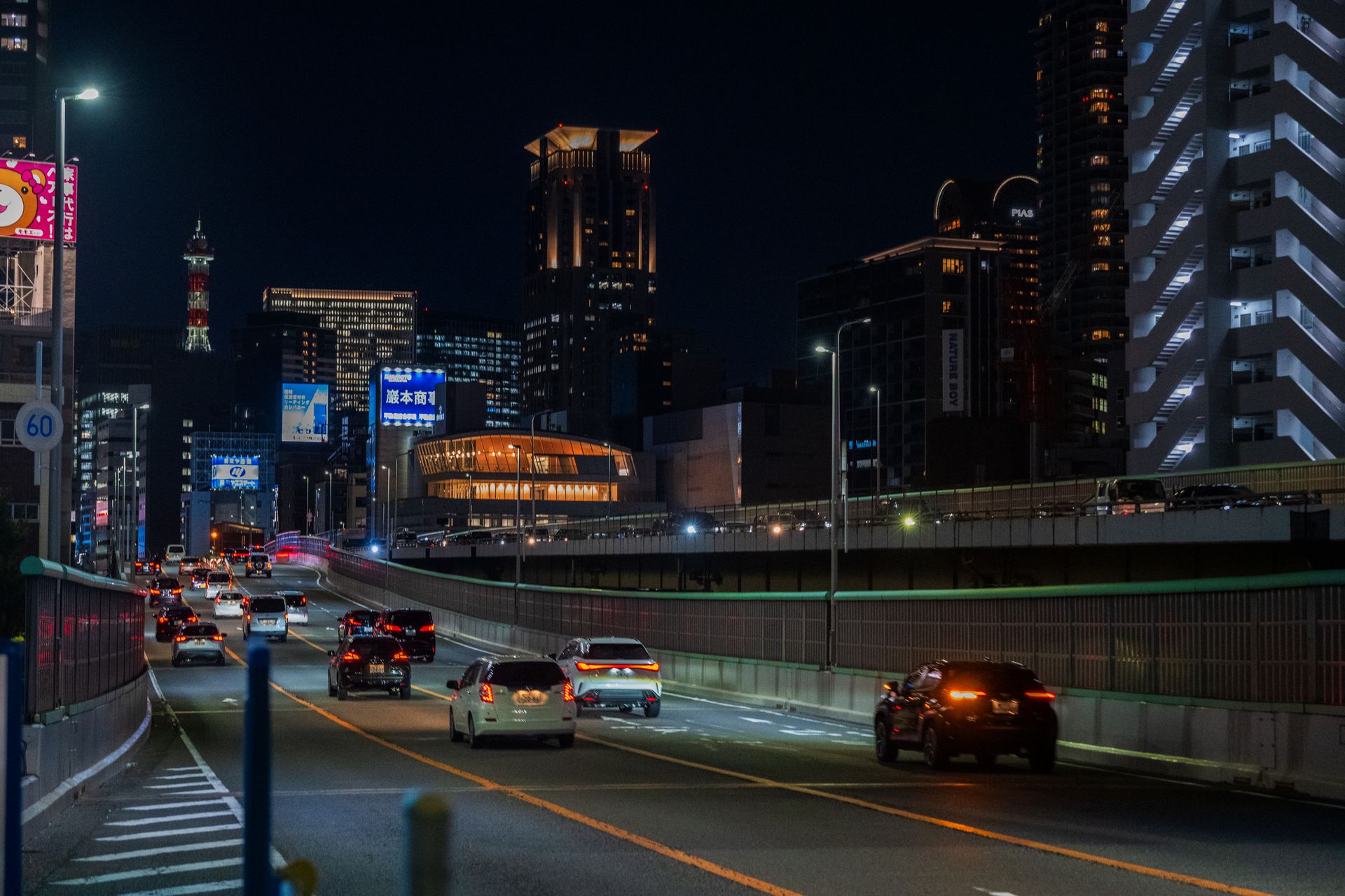 Cars driving on a highway at night with a vibrant city skyline in the background.