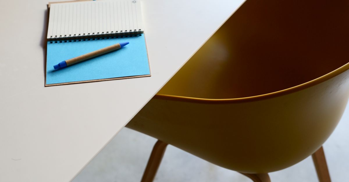 Minimalist workspace featuring a table, notebook, and modern yellow chair.