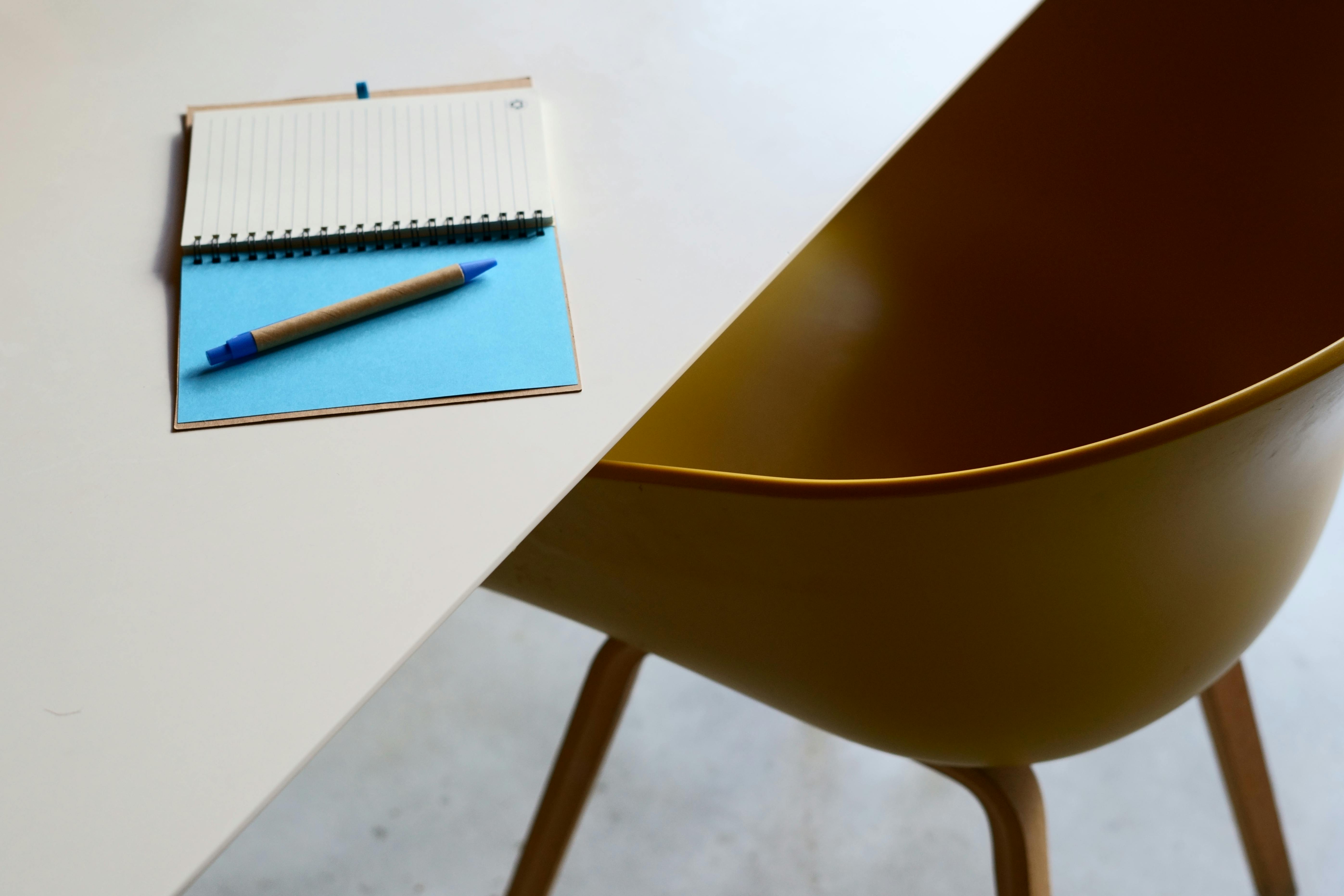 Kostenlos Minimalistischer Arbeitsbereich mit Tisch, Notizbuch und modernem gelben Stuhl. Stock-Foto