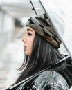 一个穿着牛仔夹克和迷彩帽的时髦妇女，在户外侧身拿着一把伞