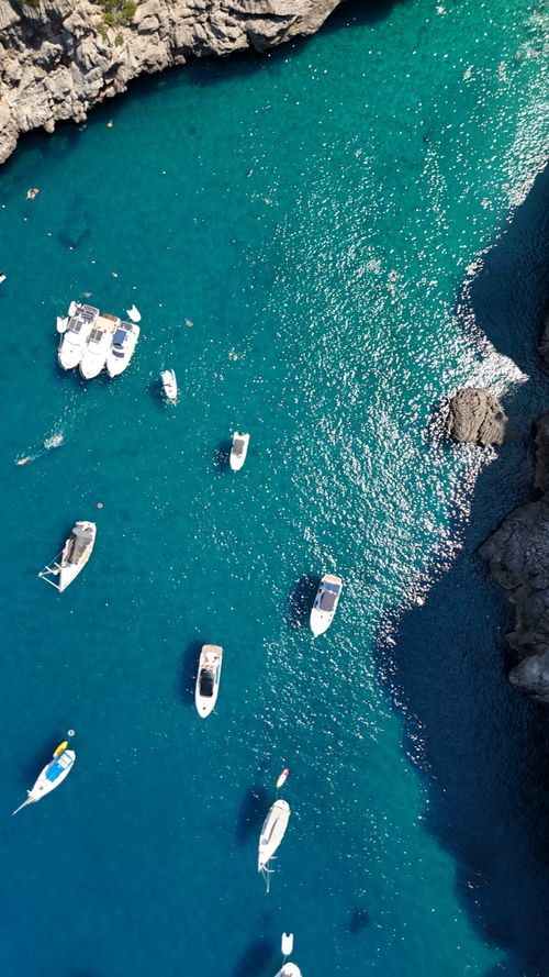Free Stunning aerial view of boats in a clear blue sea, surrounded by rocky cliffs. Stock Photo