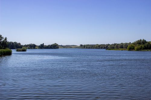 Free A serene river view surrounded by lush greenery under a clear blue sky. Stock Photo