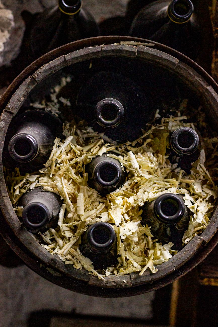 Overhead shot of wine bottles stored in a barrel with wood shavings.