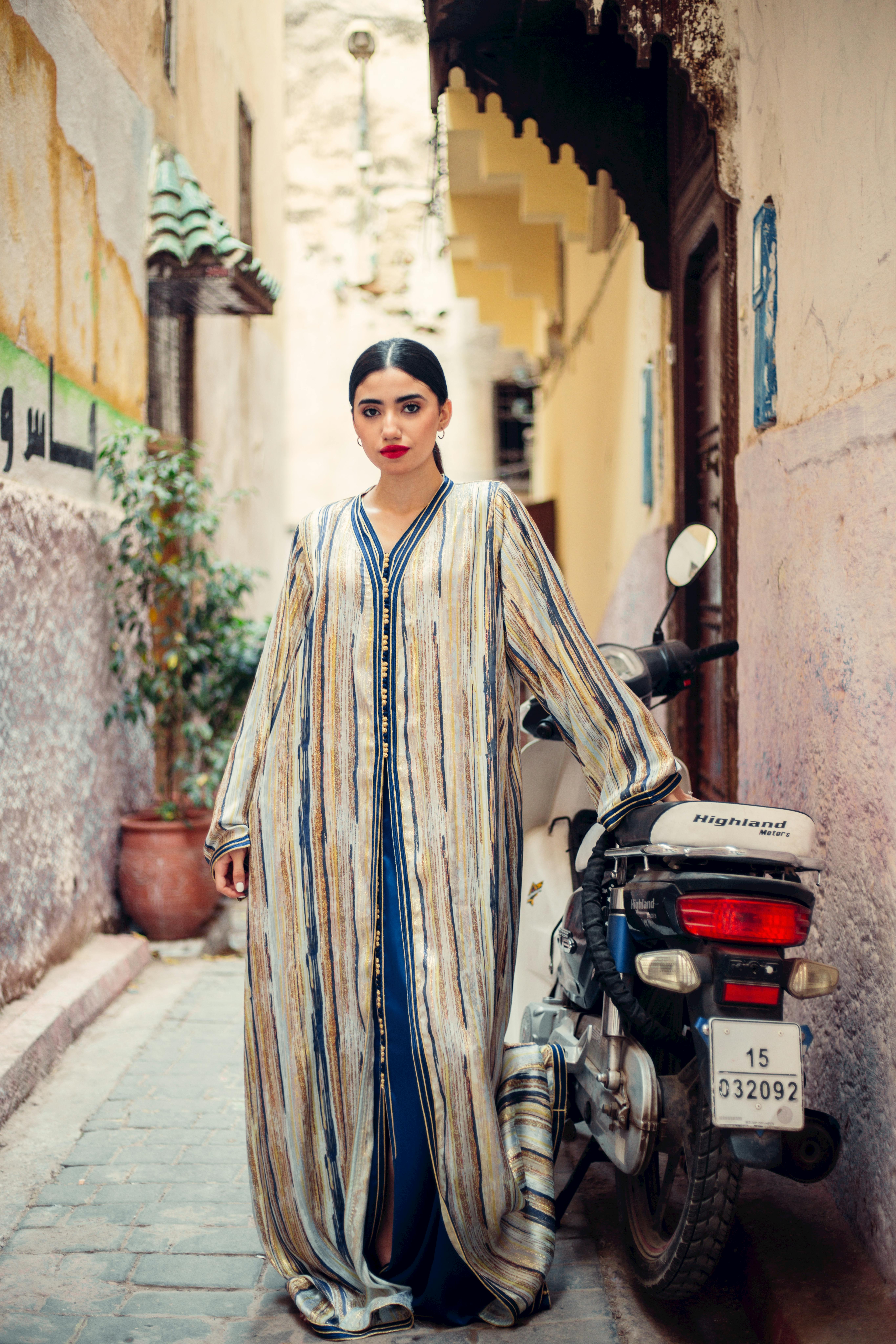 Woman in traditional Moroccan dress poses confidently in a colorful alleyway.