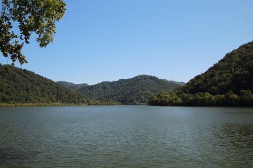 Free A tranquil view of a lake surrounded by lush green mountains on a sunny day. Stock Photo