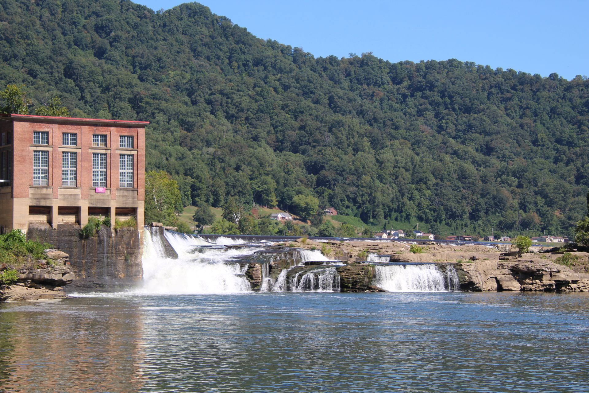 Scenic view of a hydroelectric power plant and waterfall among lush greenery.