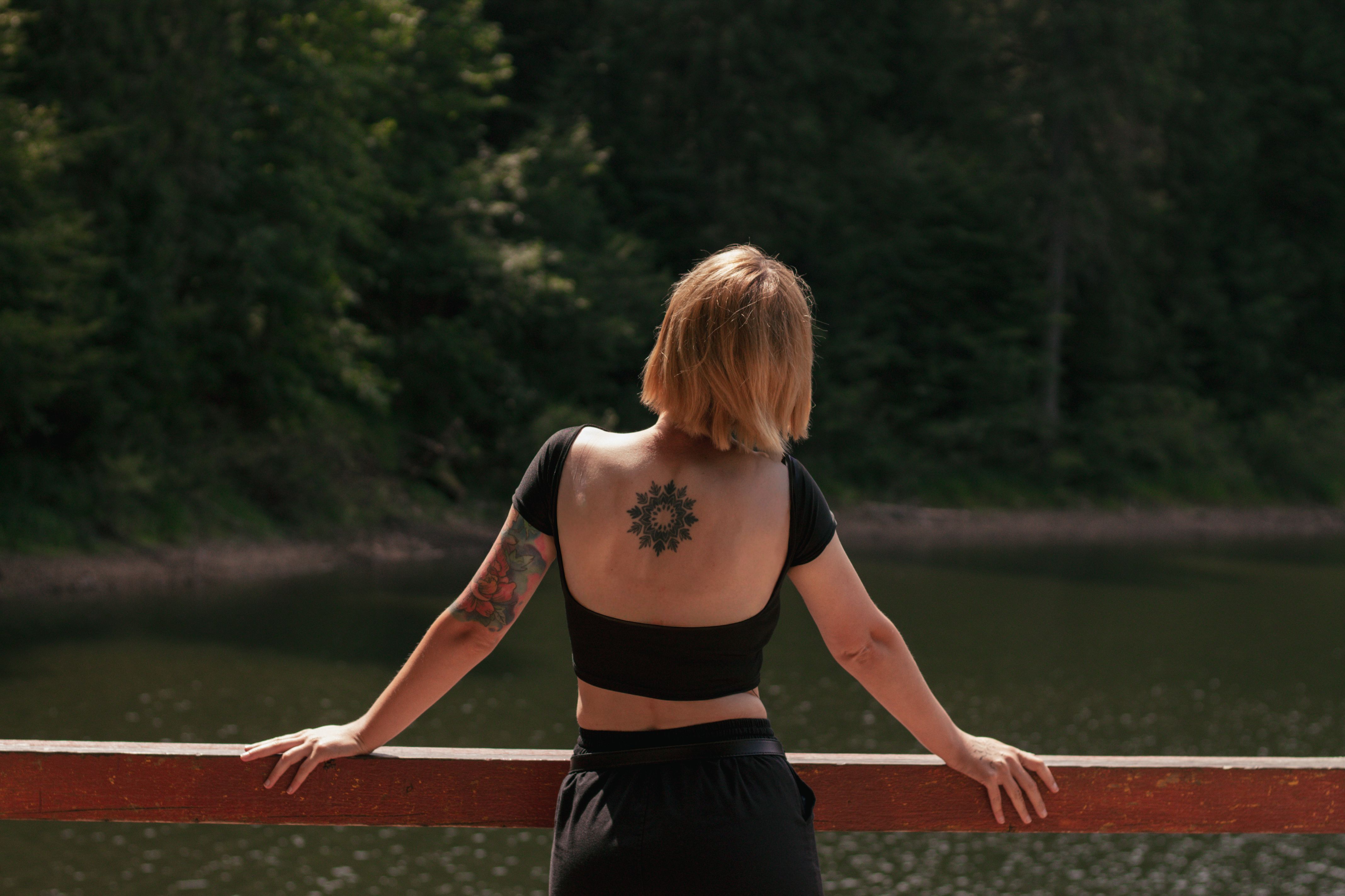 Femme tatouée d'un mandala dans le dos, face à un lac, ambiance introspection.