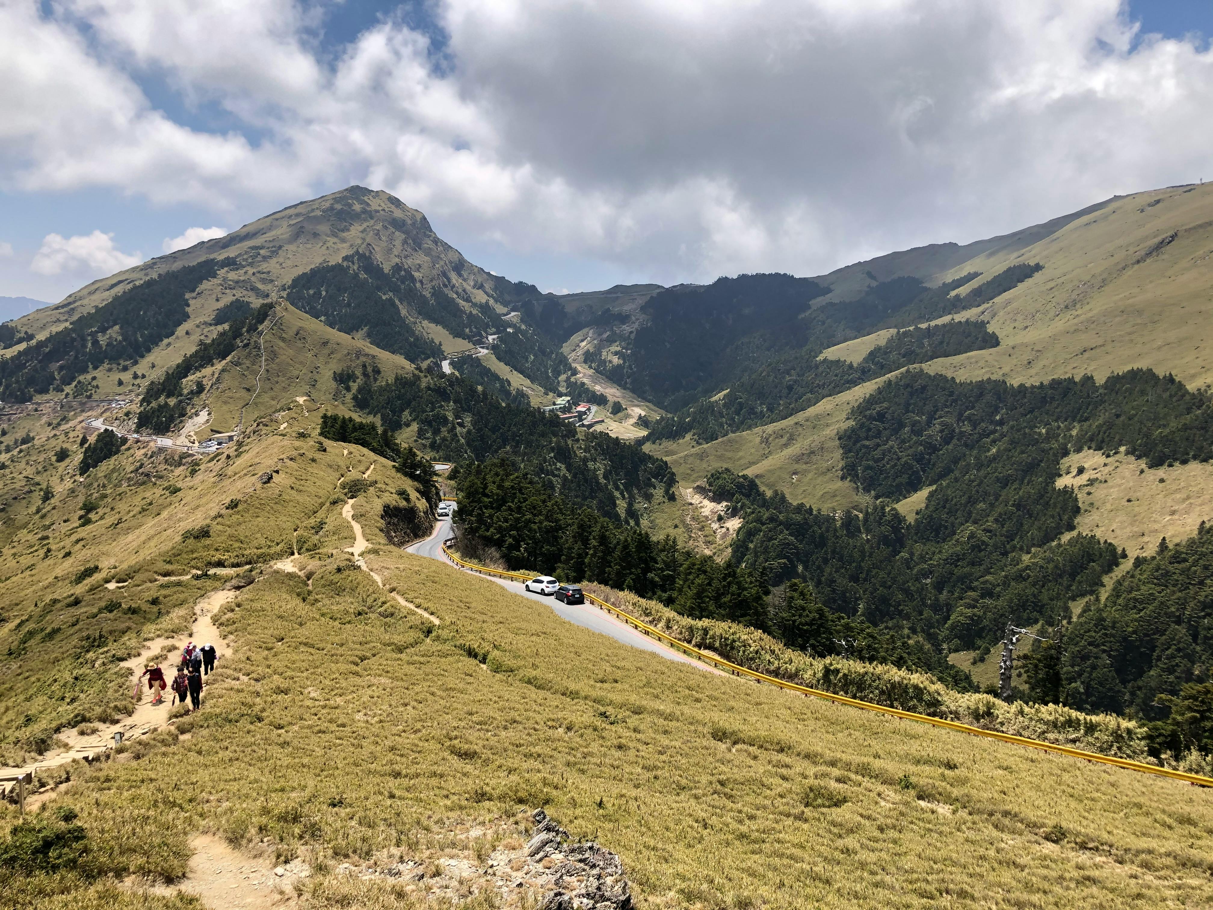 Breathtaking view of hikers on a trail in Hehuanshan, surrounded by lush mountains under a blue sky.