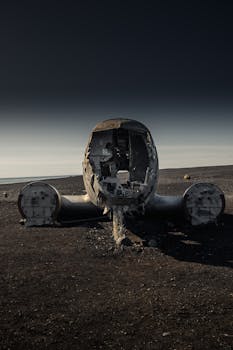Photo by Matthew DeVries Front view of a destroyed airplane wreck on barren land, under gloomy skies.