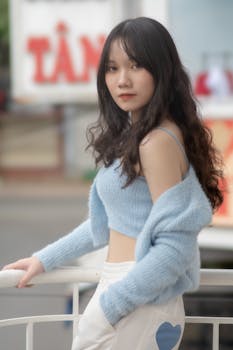 A stylish young woman poses outdoors in a chic blue sweater, showcasing casual fashion.