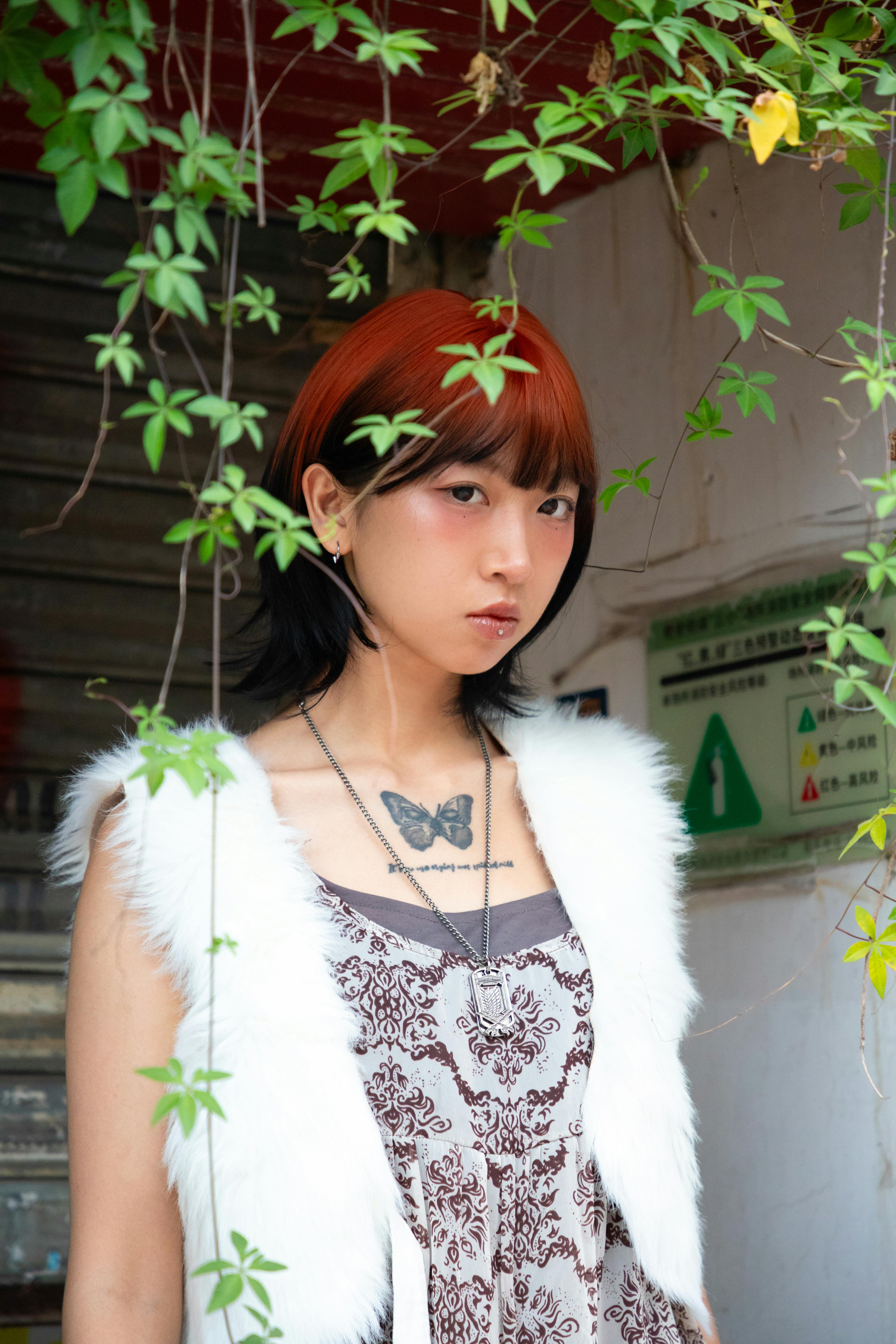 免费 带有蝴蝶纹身的年轻女子在城市环境中的树叶下摆姿势。 素材图片