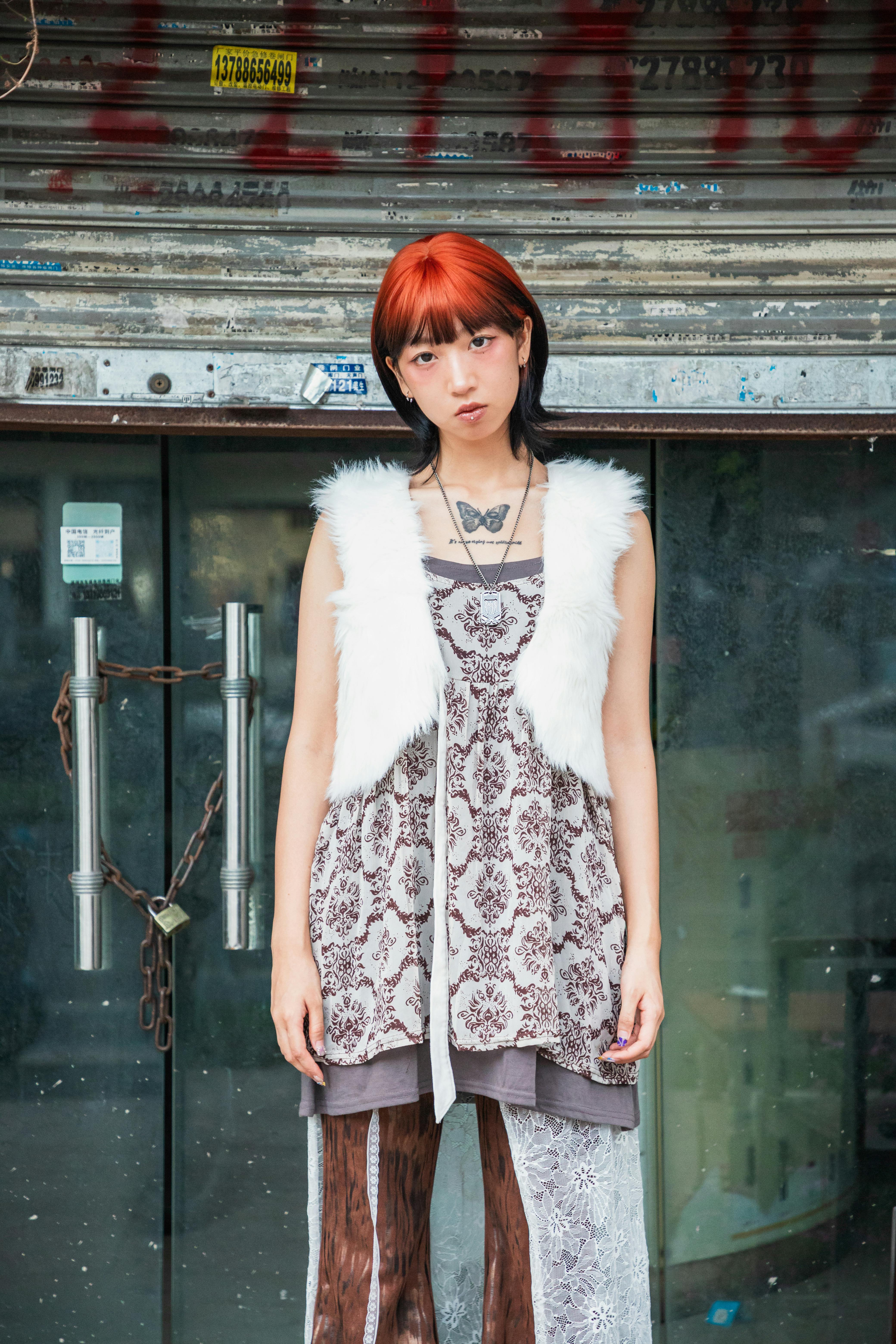 Ilmainen Tyylikäs punatukkainen ja ainutlaatuiseen muotiin pukeutunut nainen seisoo metalliportin edessä. Kuvapankkikuva