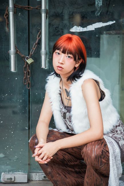 Trendy woman with striking red hair poses stylishly with urban backdrop.